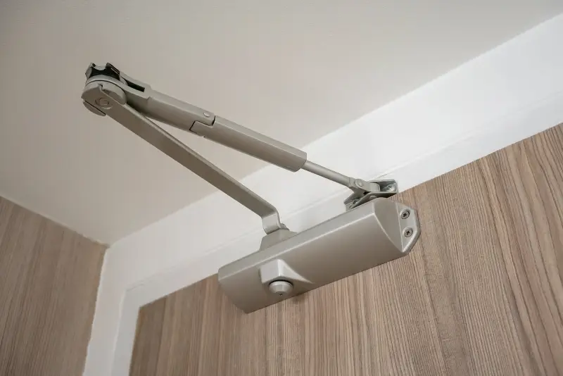 Close-up of a door closer installation, showing the mechanism mounted on the door frame for secure closing