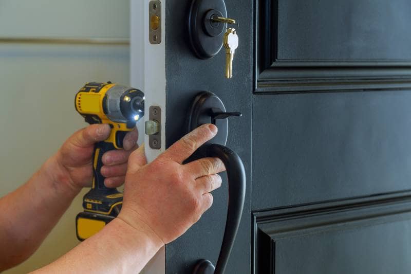 Locksmith rekeying a black front door lock using a drill, ensuring enhanced security with a new key system in Newmarket.